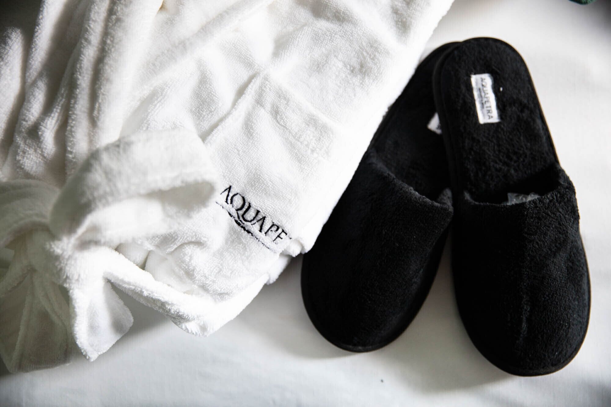 Une paire de pantoufles noires et une serviette blanche sur laquelle est inscrit le mot « AQUAFIT ».