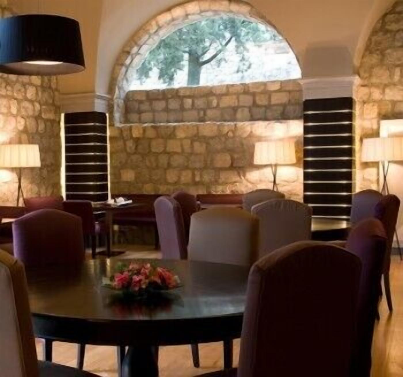 A dining area with stone walls, a large arched window, and multiple tables and chairs.