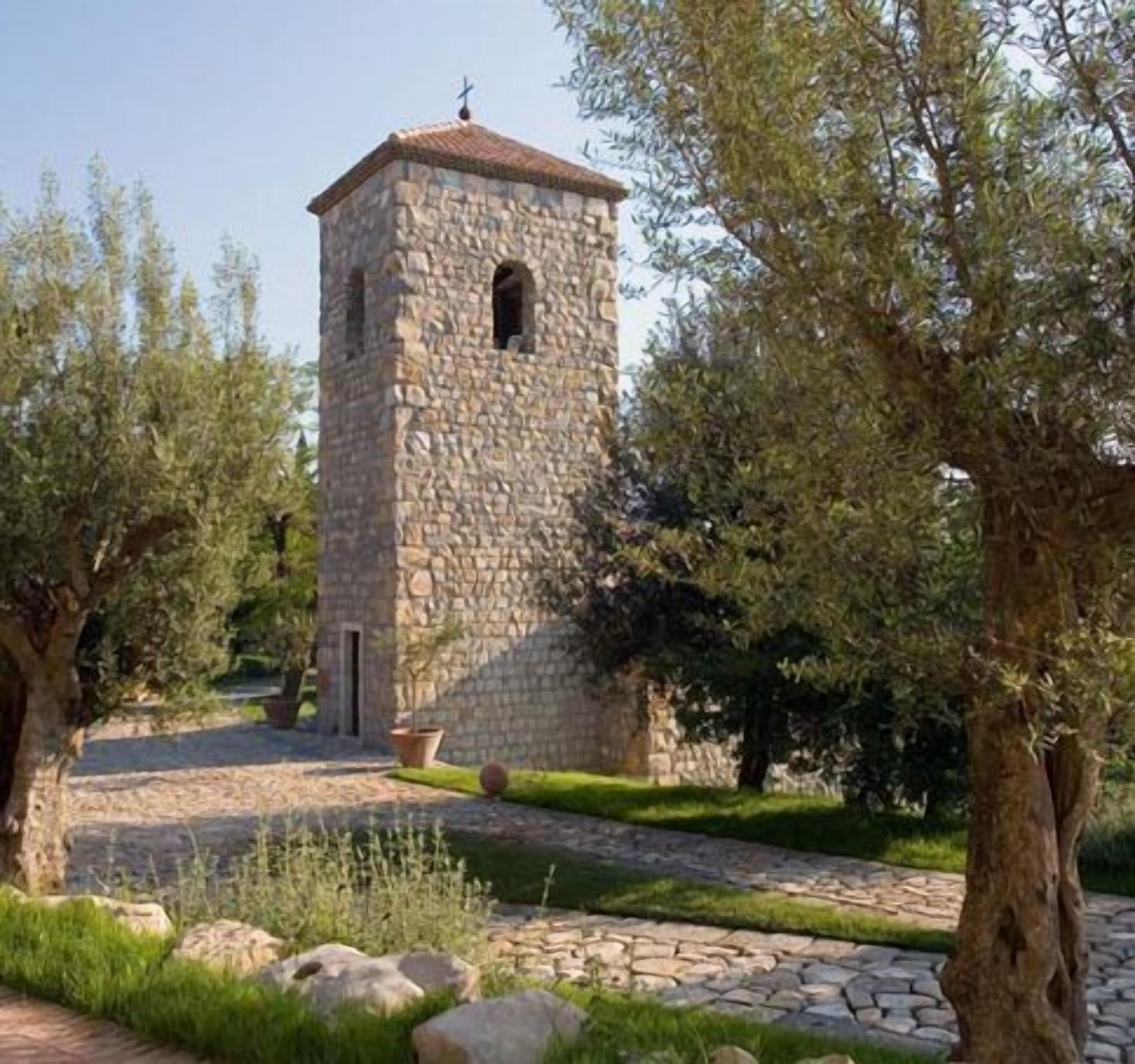 A stone tower with a cross on top, surrounded by trees and a stone pathway.
