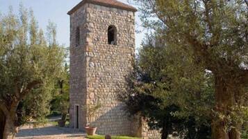 A stone tower with a cross on top, surrounded by trees and a stone pathway.