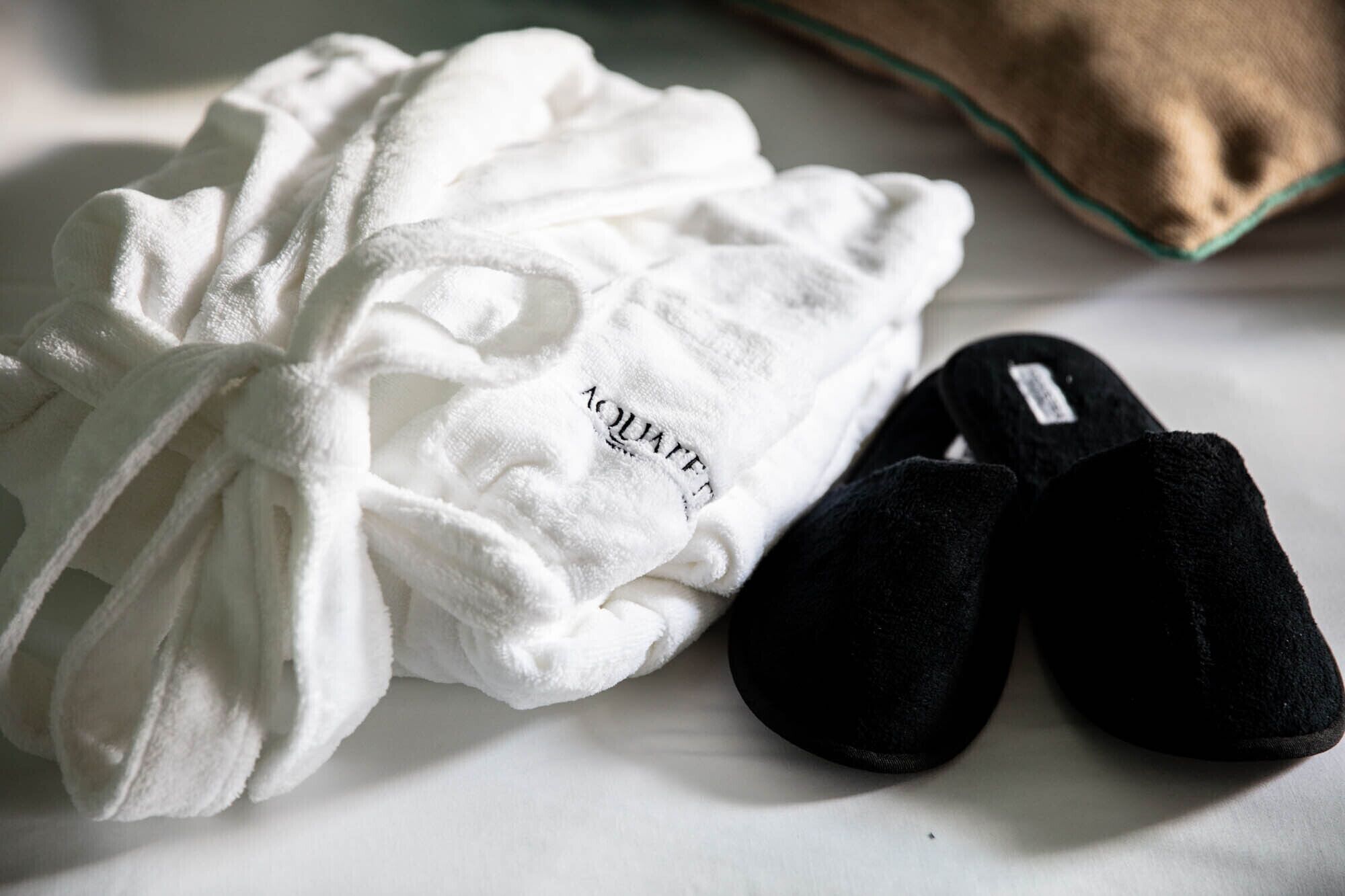Un peignoir blanc et des chaussons noirs sur un lit.