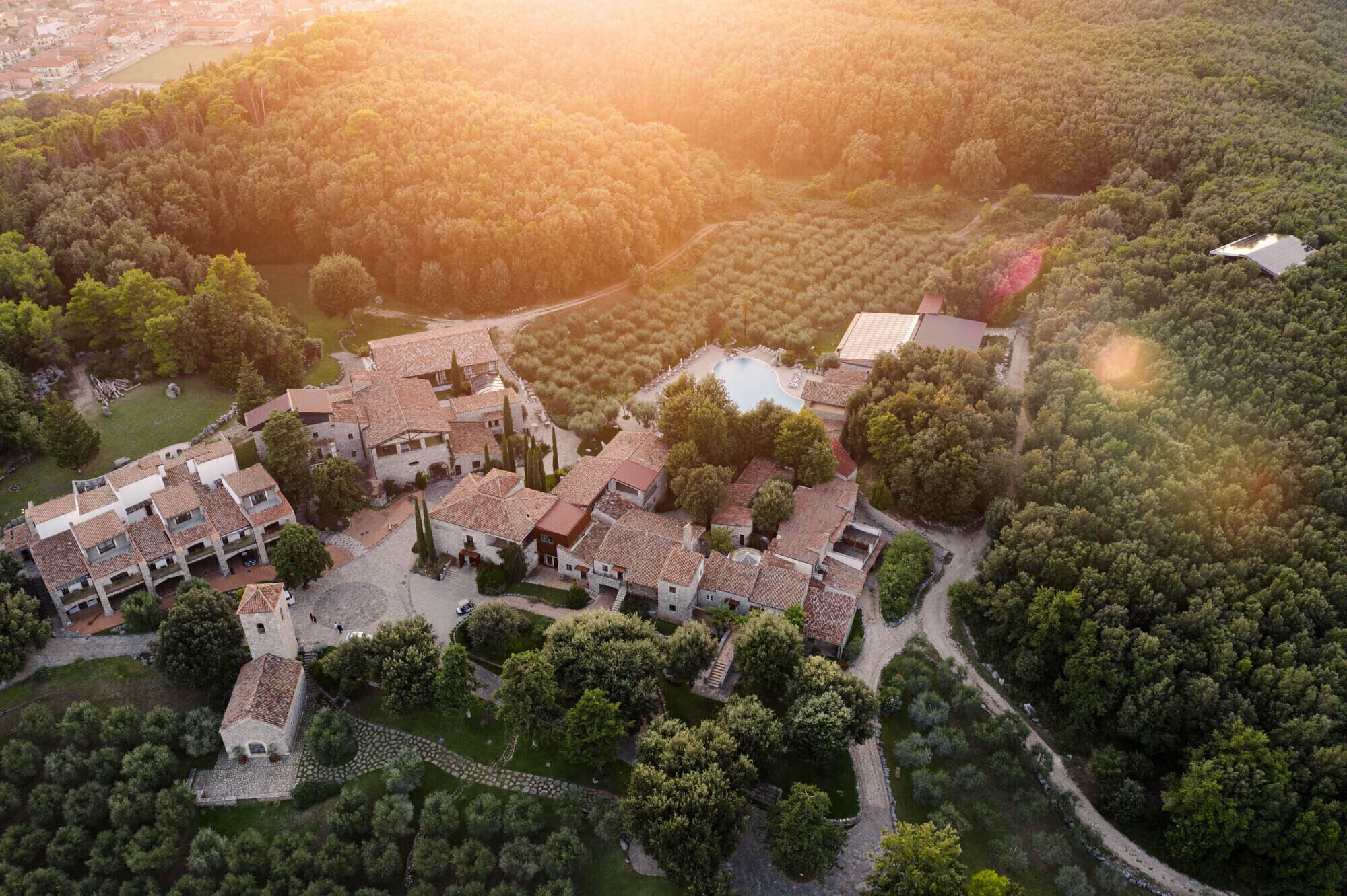 An aerial view of a resort with multiple buildings, a swimming pool, and surrounding forested areas.