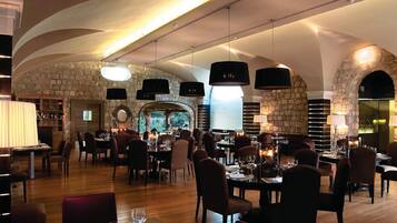 Ein Restaurant mit Steinwänden, Holztischen und schwarzen Hängelampen.