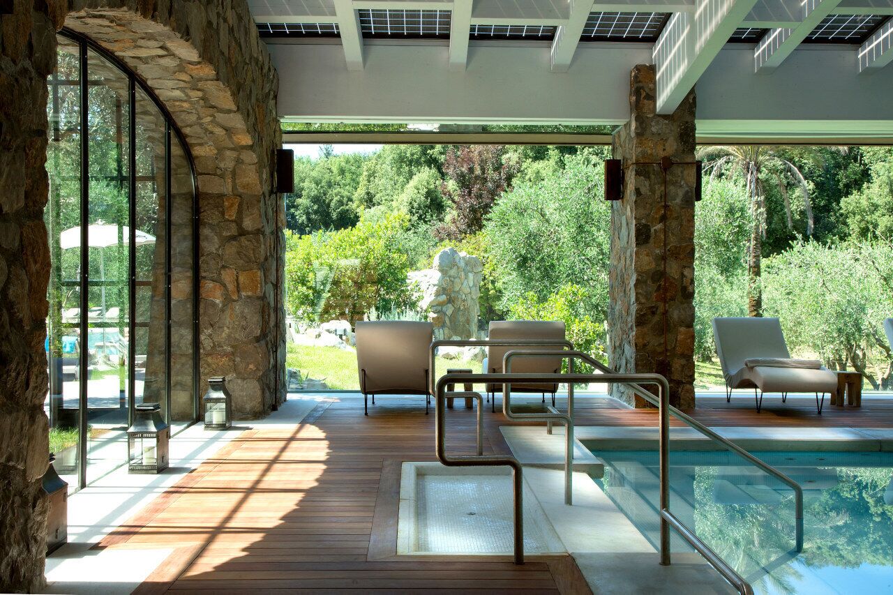 A pool area with stone pillars, lounge chairs, and a view of a lush garden.