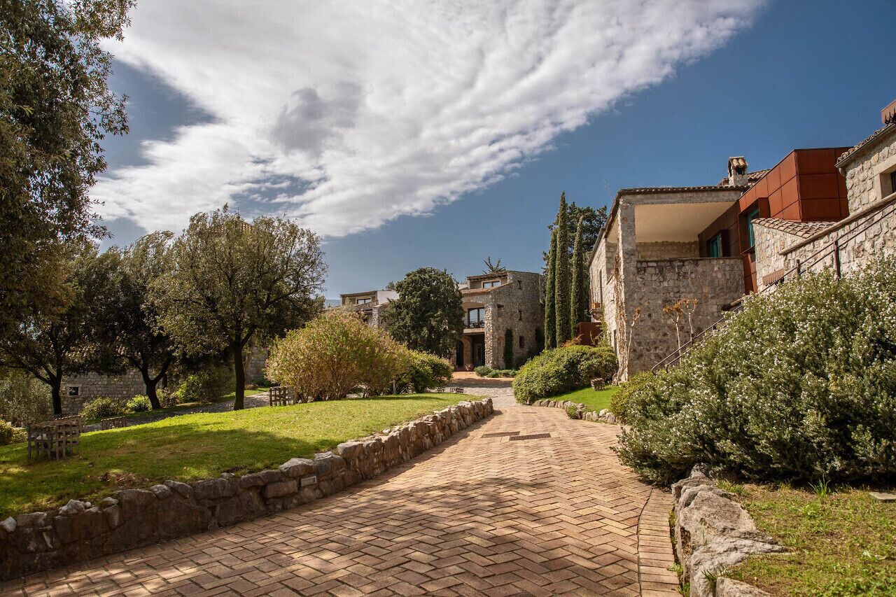 Un vialetto lastricato conduce a un edificio in pietra con giardino e alberi.