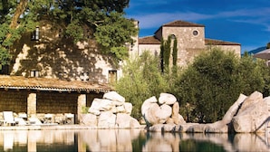 A stone building with a tiled roof, a pool with rocks, and lounge chairs. - Aquapetra Resort and Spa (Telese)