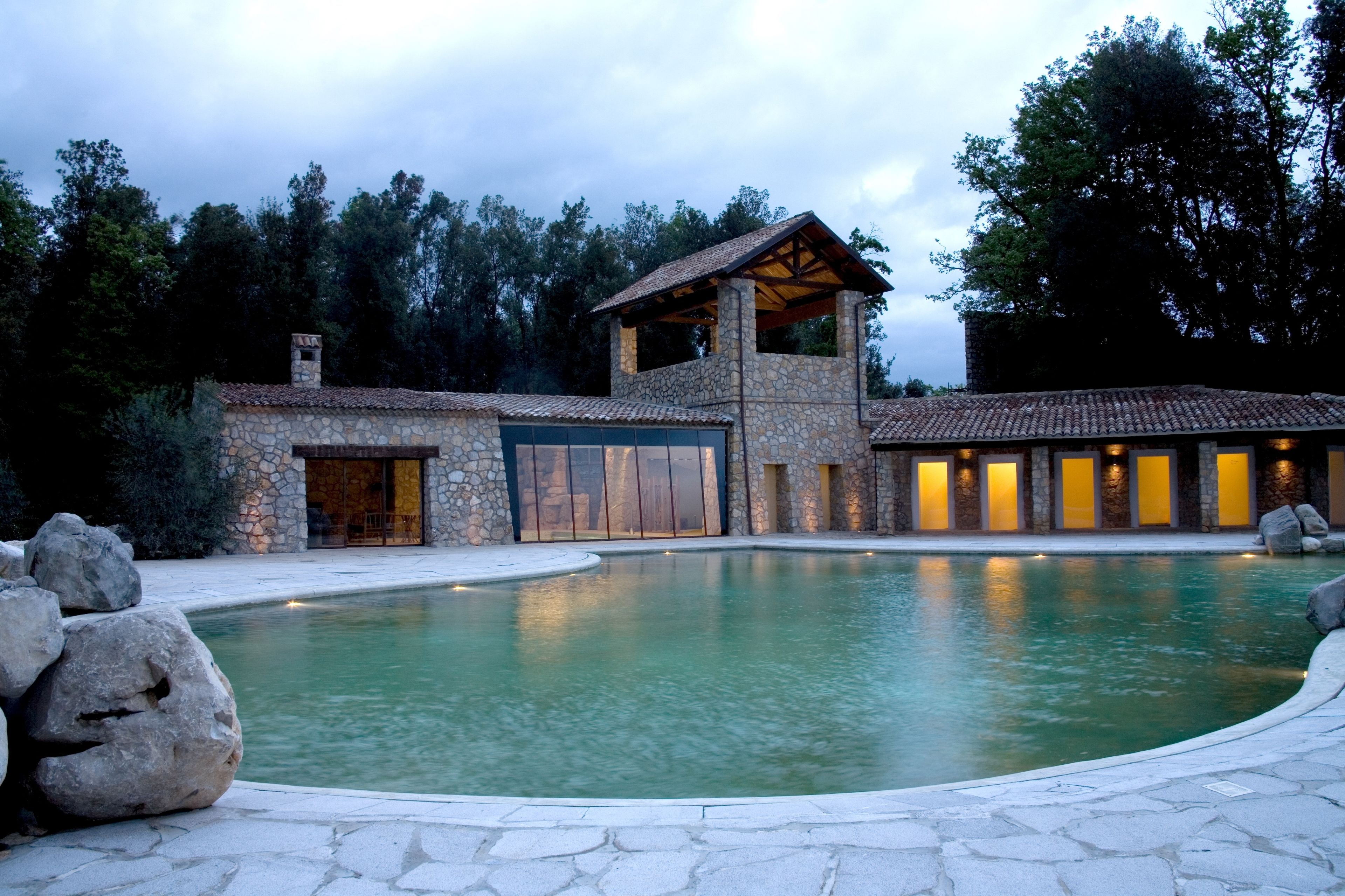 A stone building with a swimming pool, large rocks, and a forested background.