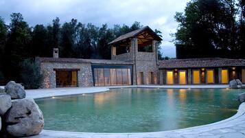 A stone building with a swimming pool, large rocks, and a forested background.