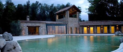 A stone building with a swimming pool, large rocks, and a forested background.