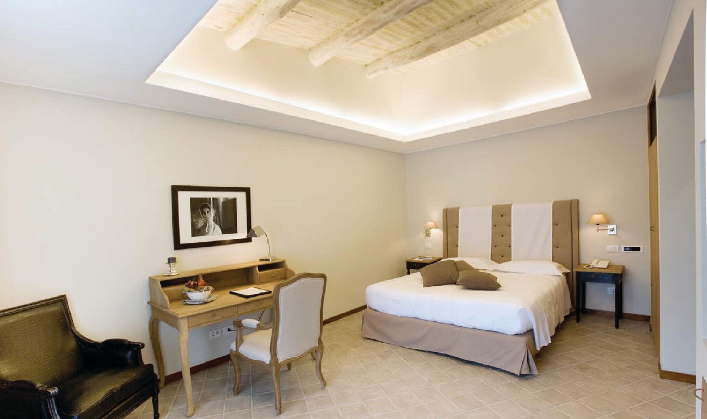 A hotel room with a bed, desk, chair, and a framed picture on the wall.
