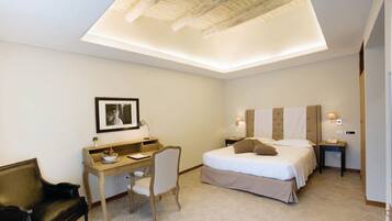 A hotel room with a bed, desk, chair, and a framed picture on the wall.