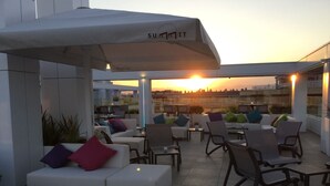 An outdoor seating area with white sofas and chairs, some with colorful cushions, under a large umbrella with the logo "SUMMIT IT". - Olympus Palace (Salou)