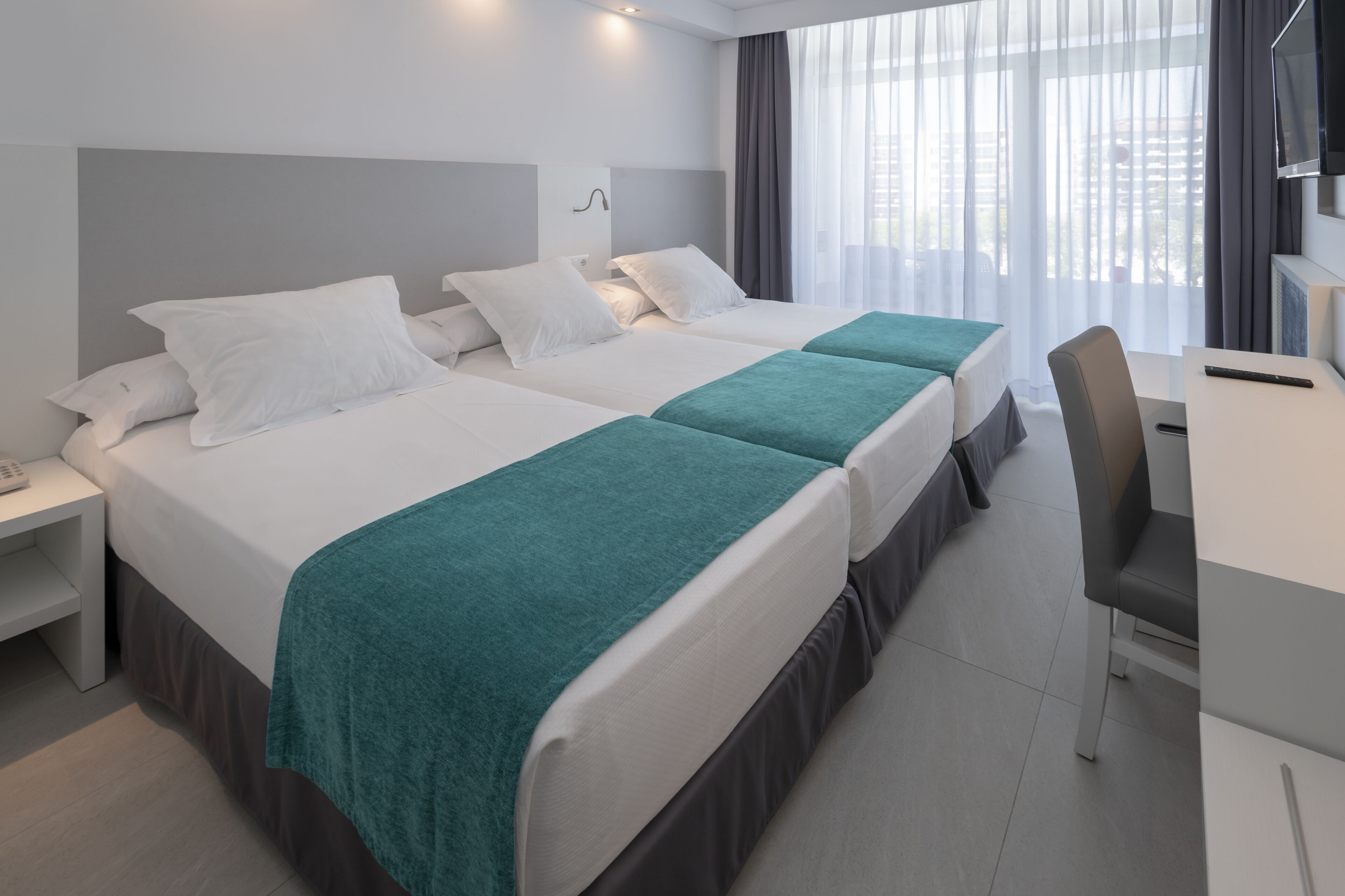 A hotel room with two beds, a desk, and a TV.