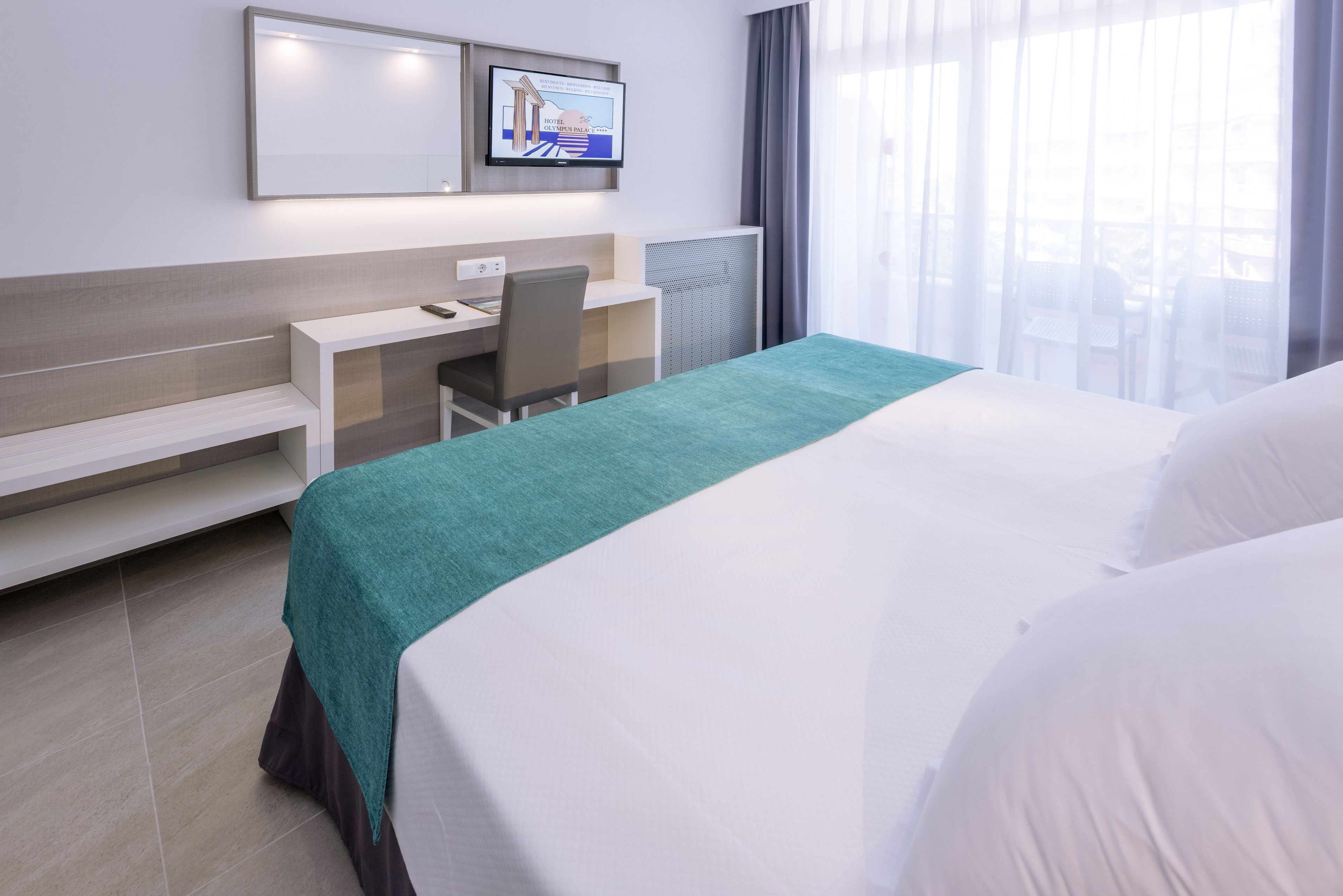 Een hotelkamer met een bed, een bureau, een stoel, een televisie aan de muur en een raam met gordijnen.