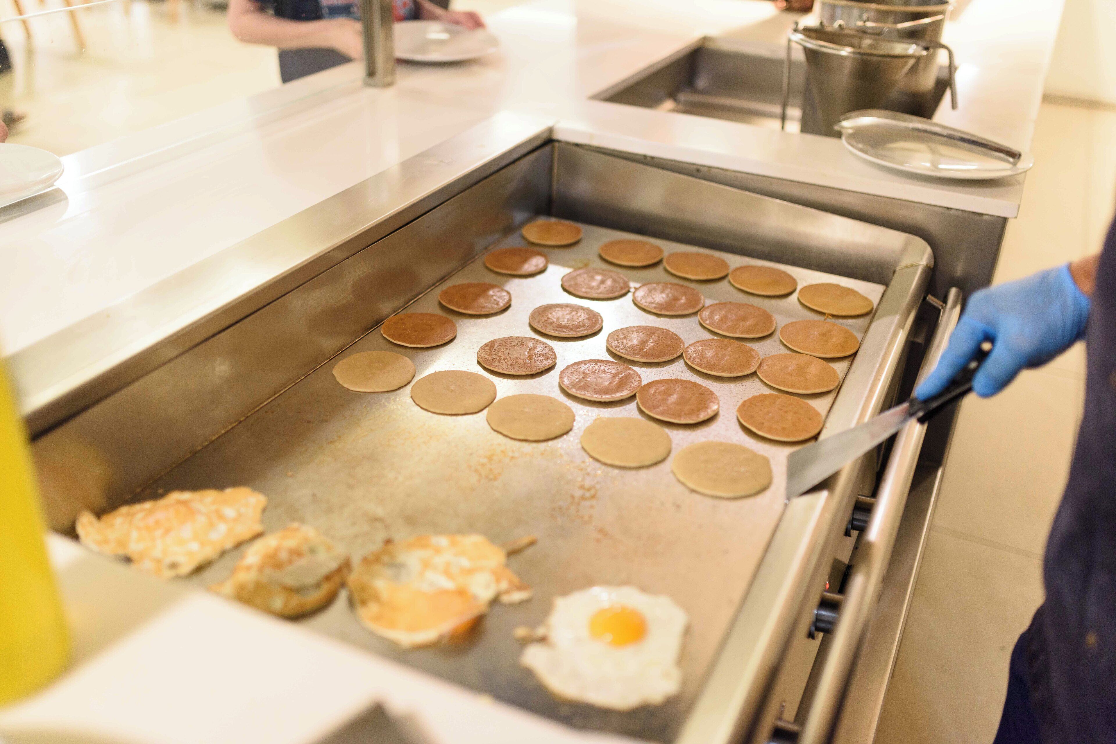 Pancakes being cooked on a griddle with a person flipping them.