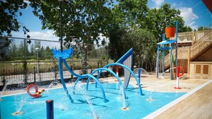 Een waterpretplaats met een zwembad, blauwe speeltoestellen en een houten terras.