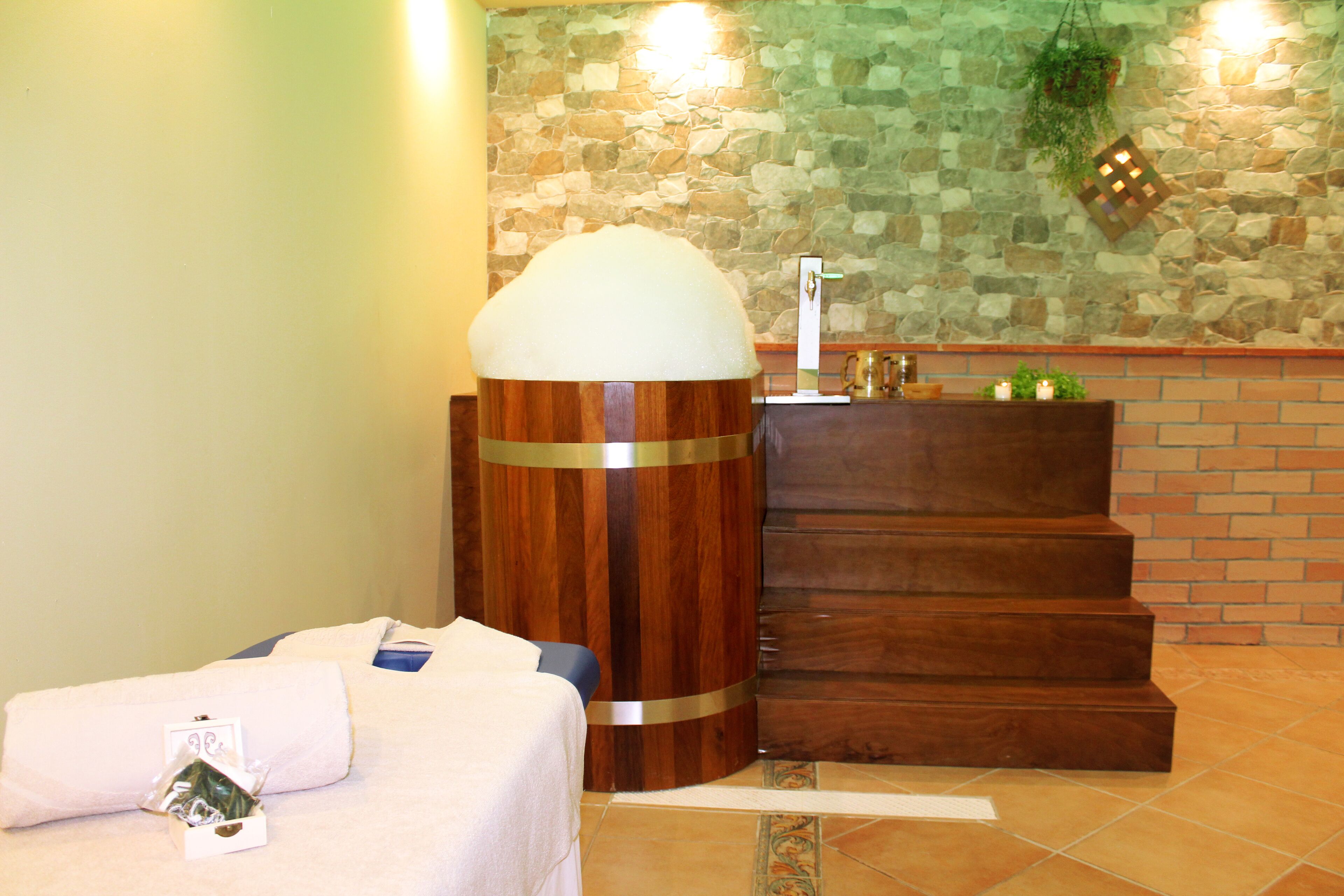 A bathroom with a stone wall, a wooden stool with a white object on top, and a brick wall with a wooden counter.