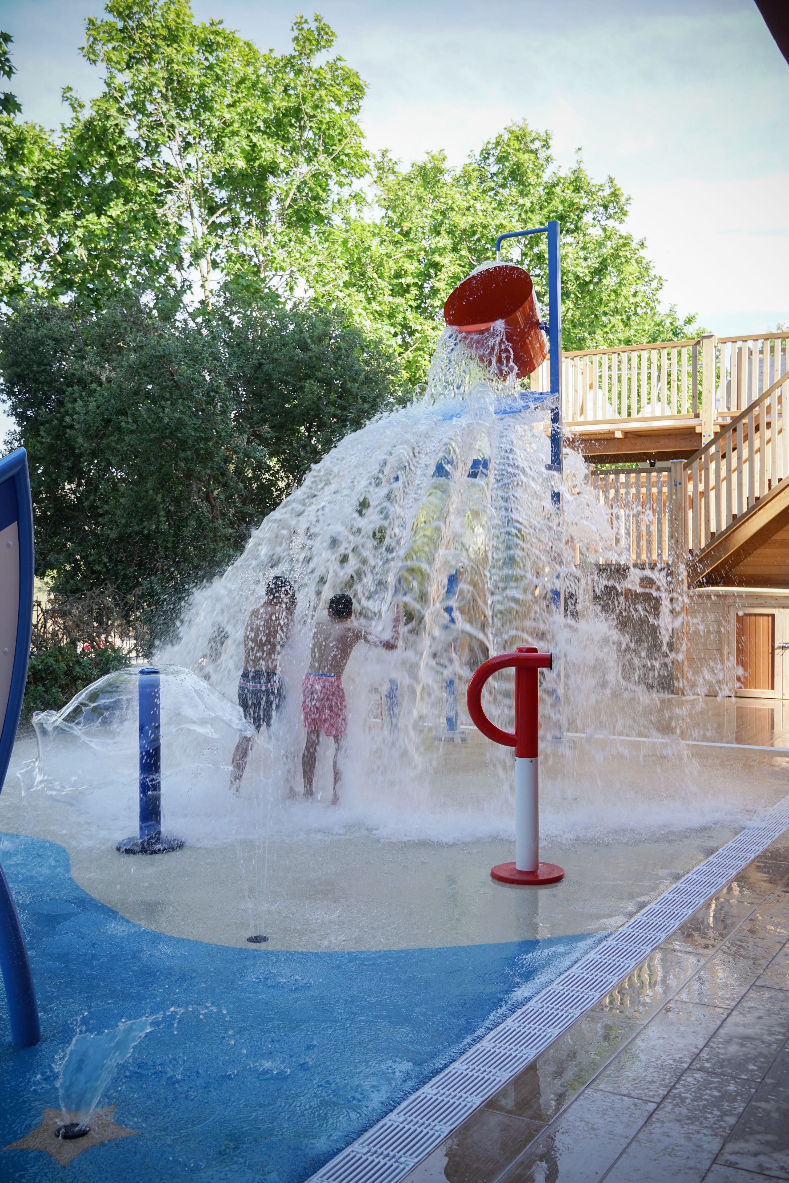 Un área de juegos acuáticos con múltiples chorros de agua y una terraza de madera al fondo.