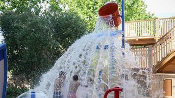 Un área de juegos acuáticos con múltiples chorros de agua y una terraza de madera al fondo.
