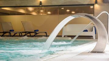 Una piscina interior con agua cristalina, un elemento acuático y sillones de descanso a un lado.