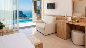 A modern hotel room with a balcony overlooking a scenic ocean view, a comfortable seating area, and a wooden vanity with a mirror.
