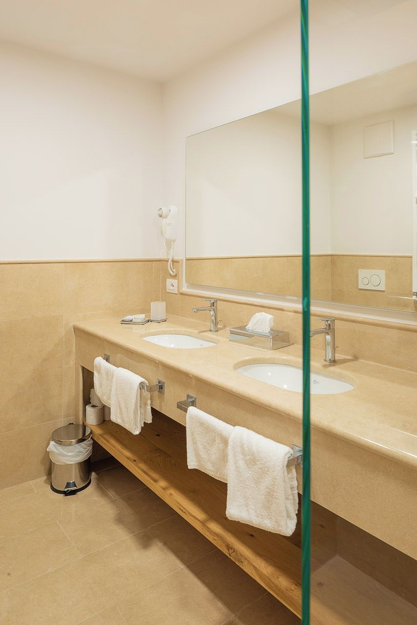 Een moderne badkamer met drie wasbakken, een grote spiegel en een glazen douchewand.