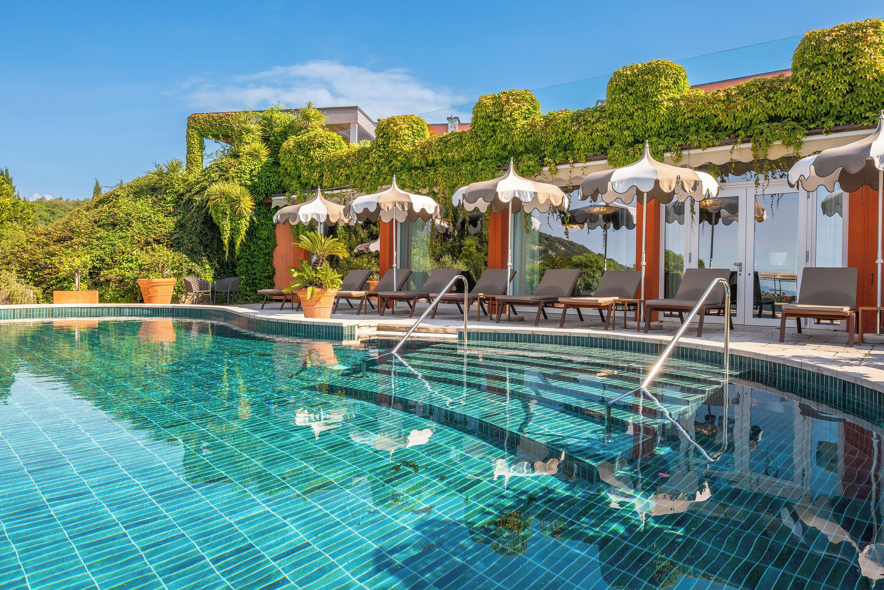 A swimming pool with tiled steps, lounge chairs, and umbrellas.