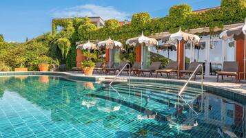 A swimming pool with tiled steps, lounge chairs, and umbrellas.