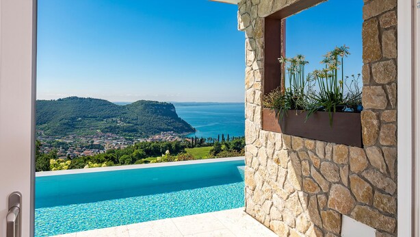 A stone wall with a built-in planter and a clear view of a coastal town and mountains.