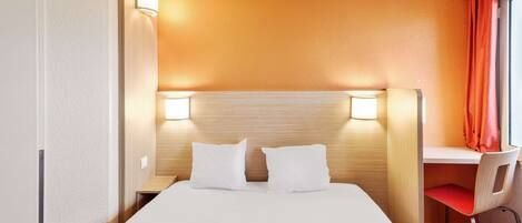 Una habitación de hotel con cama, dos lámparas de noche, un escritorio con silla y una ventana con cortinas.