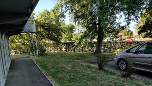 Ein Parkplatz mit befestigtem Weg, einem geparkten Auto und einer Hecke im Hintergrund.
