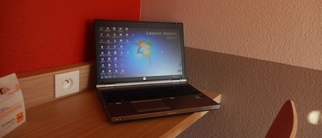 Una computadora portátil sobre un escritorio de madera, con una pared beige y roja al fondo.