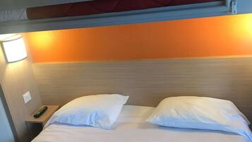 A bunk bed with two white pillows, a red quilted blanket, and a bedside table with a remote control.
