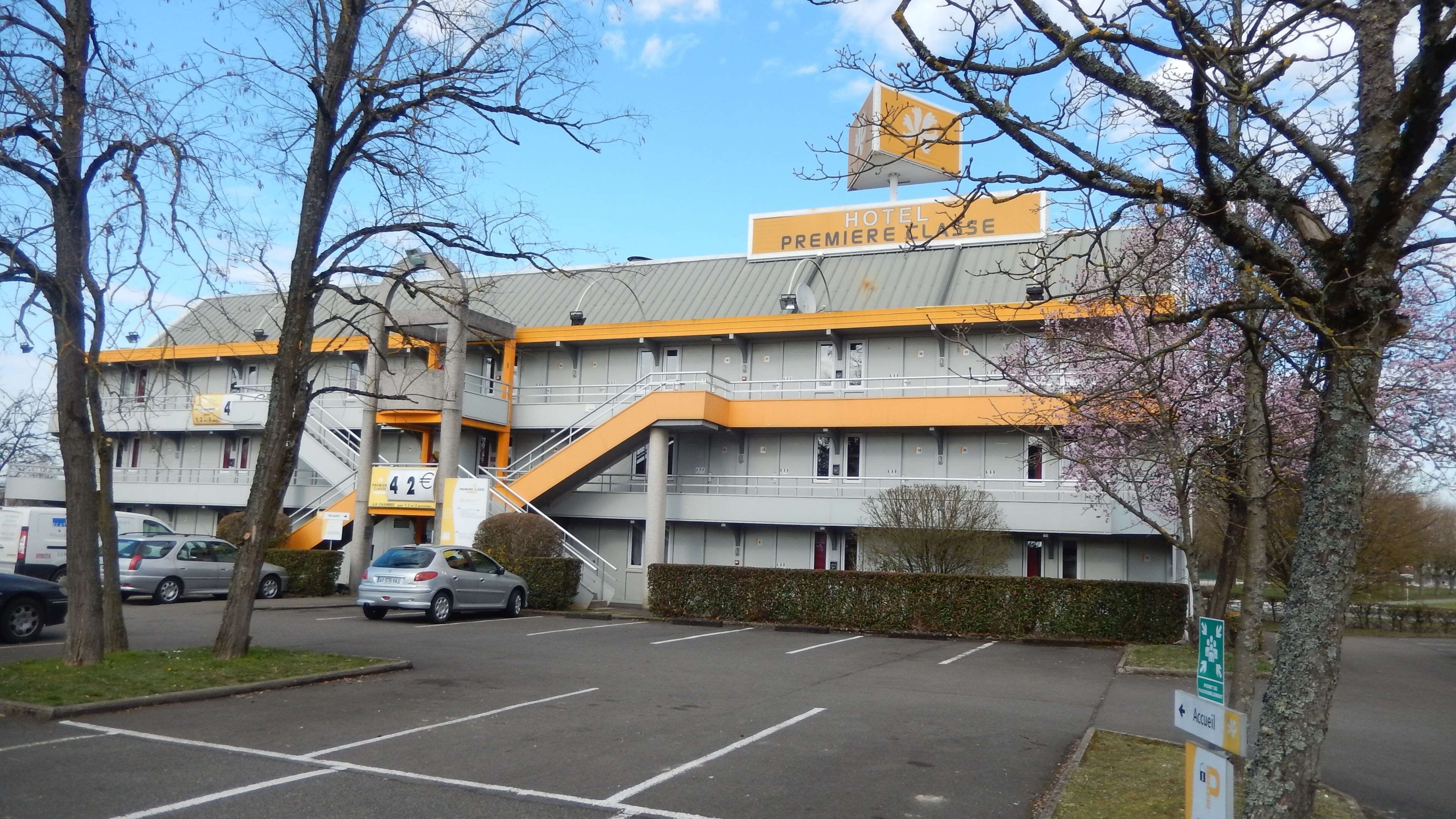 A hotel with a modern architectural design, featuring a prominent yellow and grey color scheme, a visible entrance, and a parking lot in front.