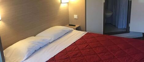 A hotel room with a bed, a nightstand, and a wall-mounted light fixture.