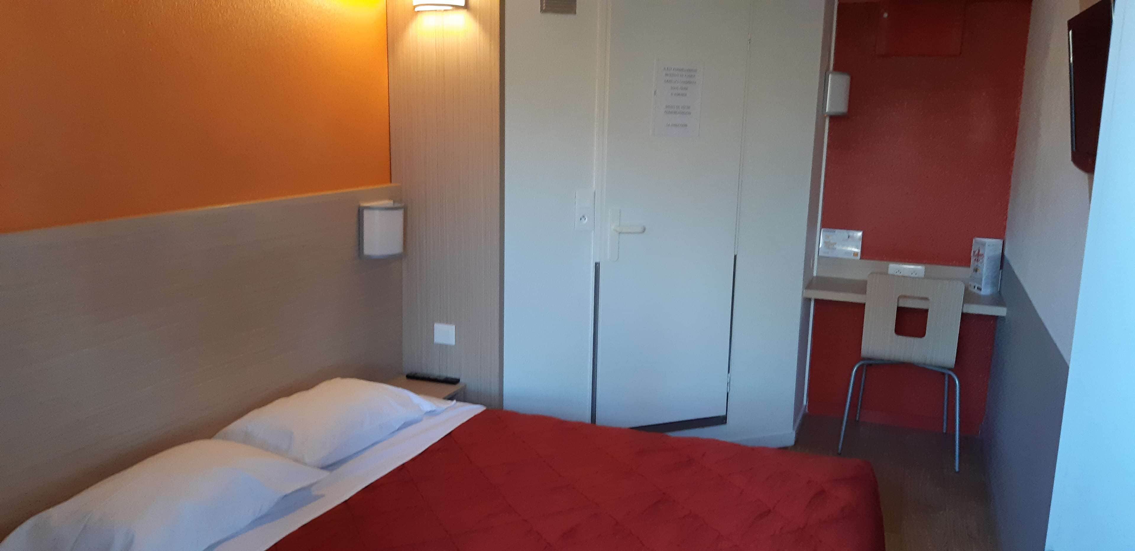 A compact hotel room with a single bed, a small desk, and a chair.