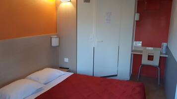 A compact hotel room with a single bed, a small desk, and a chair.