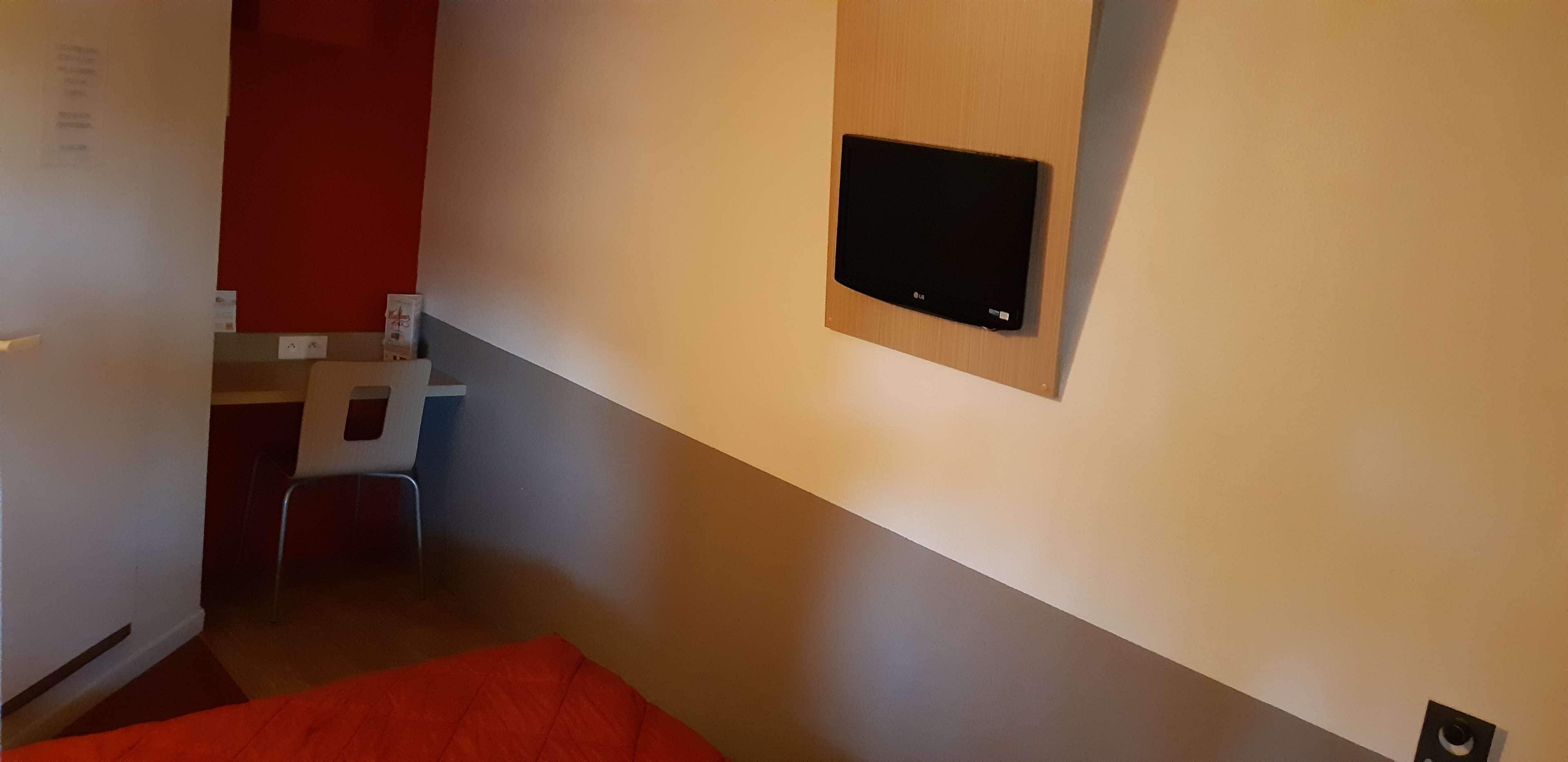 Quarto de hotel com cama, escrivaninha e televisão na parede.