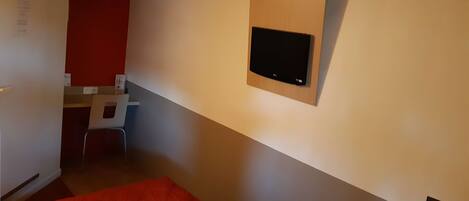 Habitación de hotel con cama, escritorio y televisor montado en la pared.