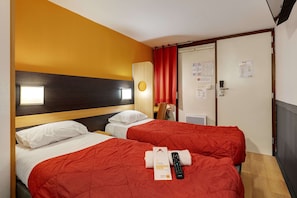 Two single beds with red quilted bedspreads and white pillows, a wooden headboard, and a wall-mounted light fixture.