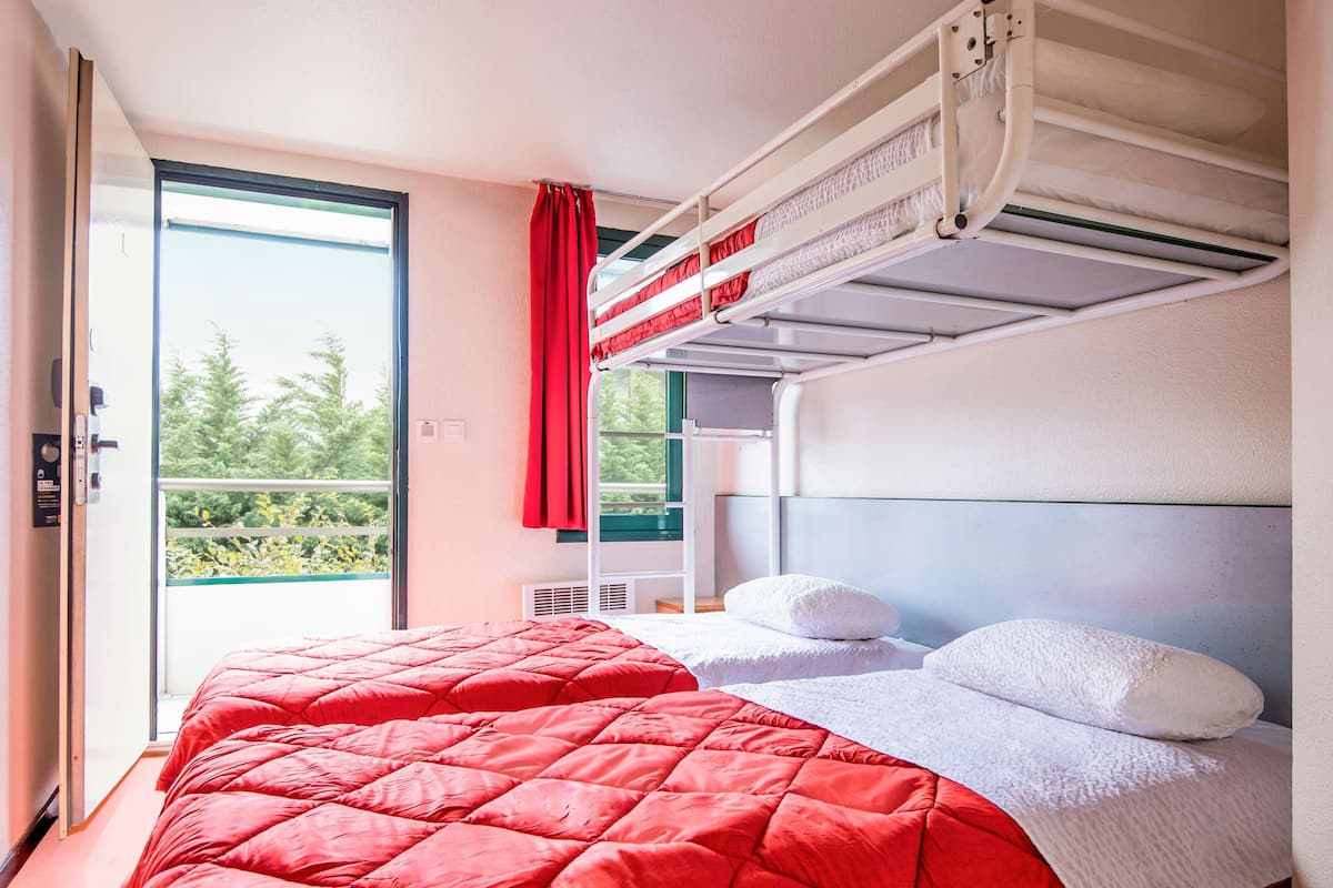 Une chambre avec un lit superposé, une couvre-lit rouge, des oreillers blancs et une vue sur la verdure.