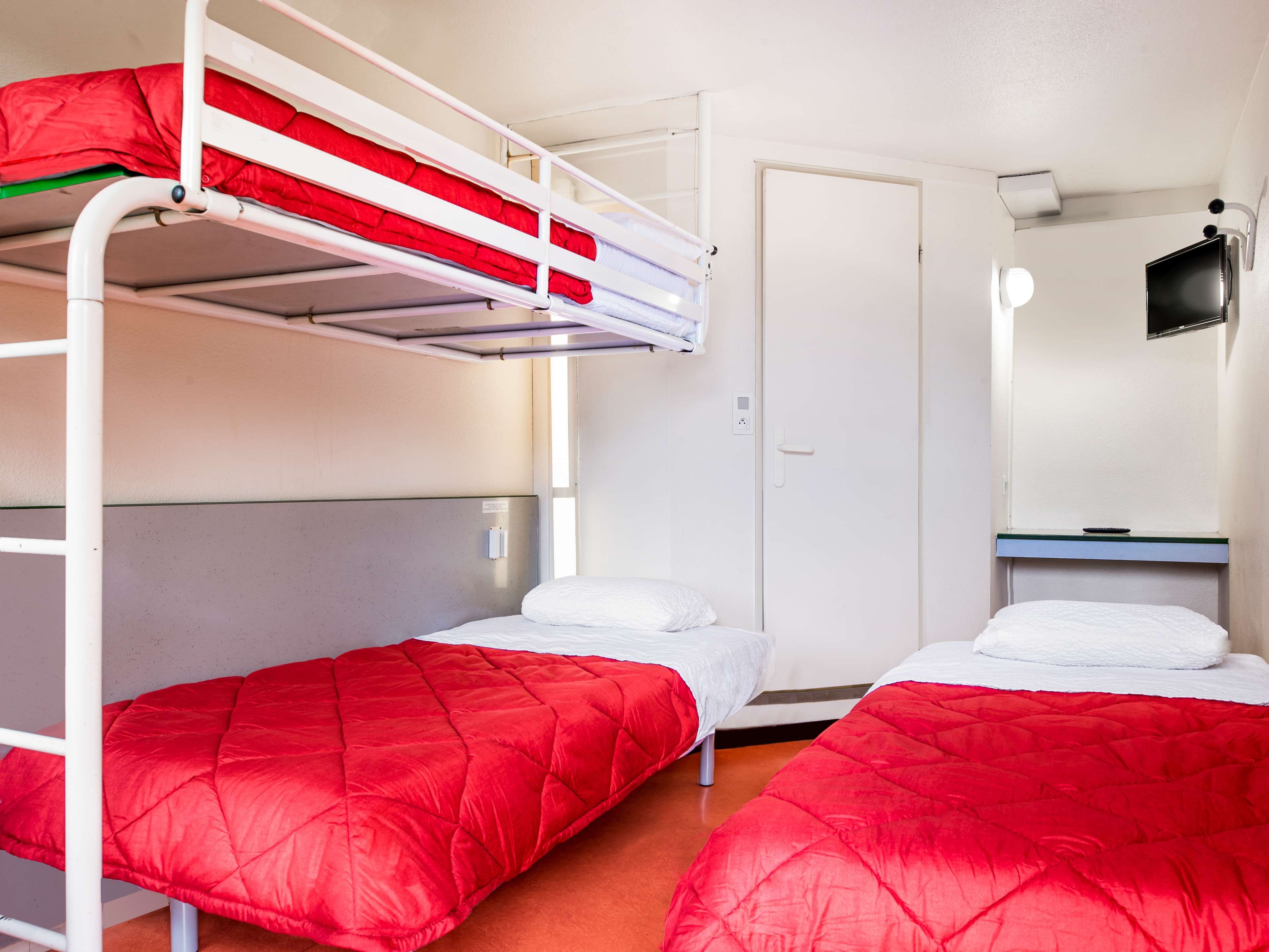 A bunk bed room with two beds, a door, a small desk, and a television.