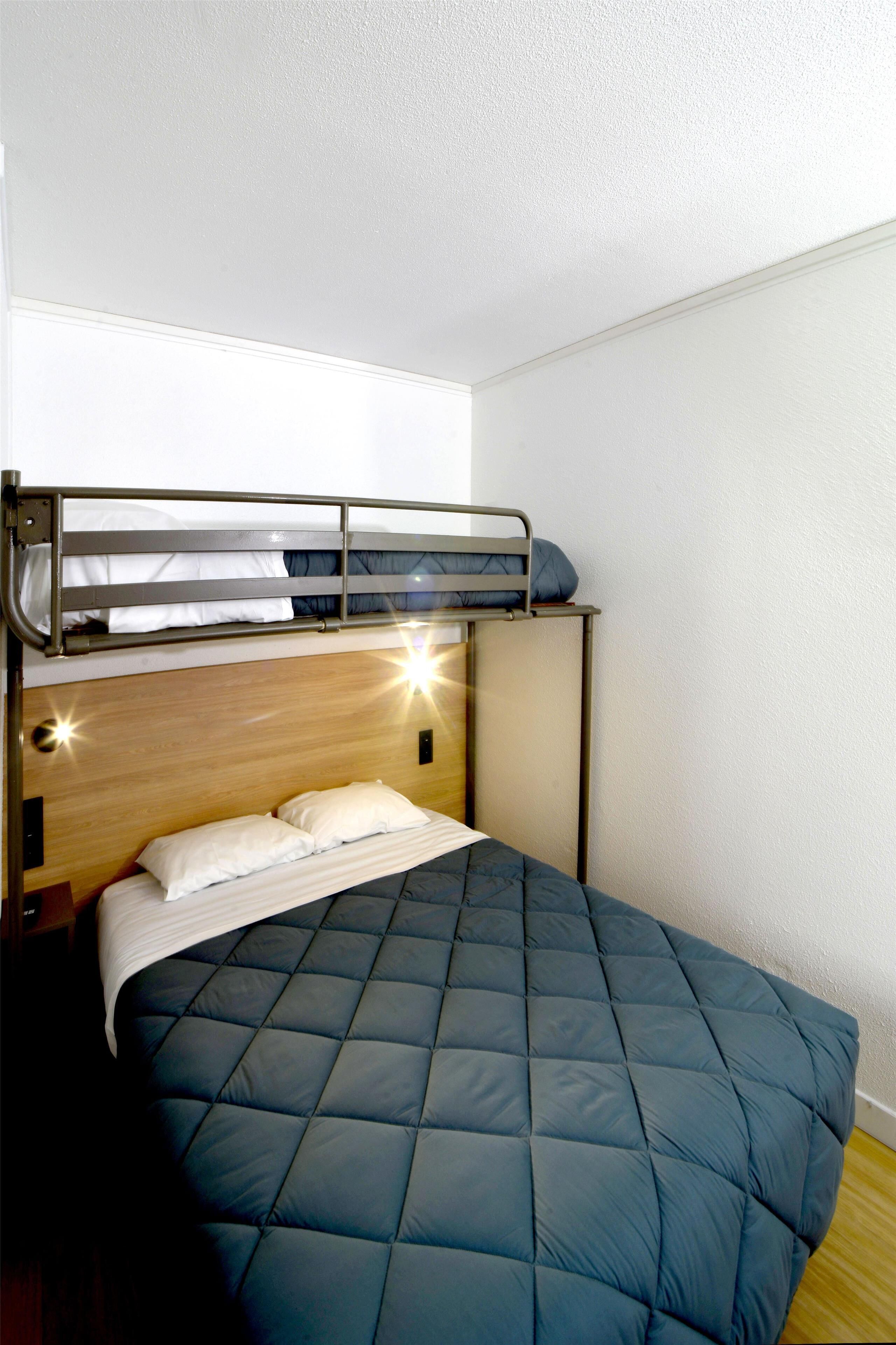 Un lit superposé avec un matelas matelassé bleu, une tête de lit en bois et une structure en métal.