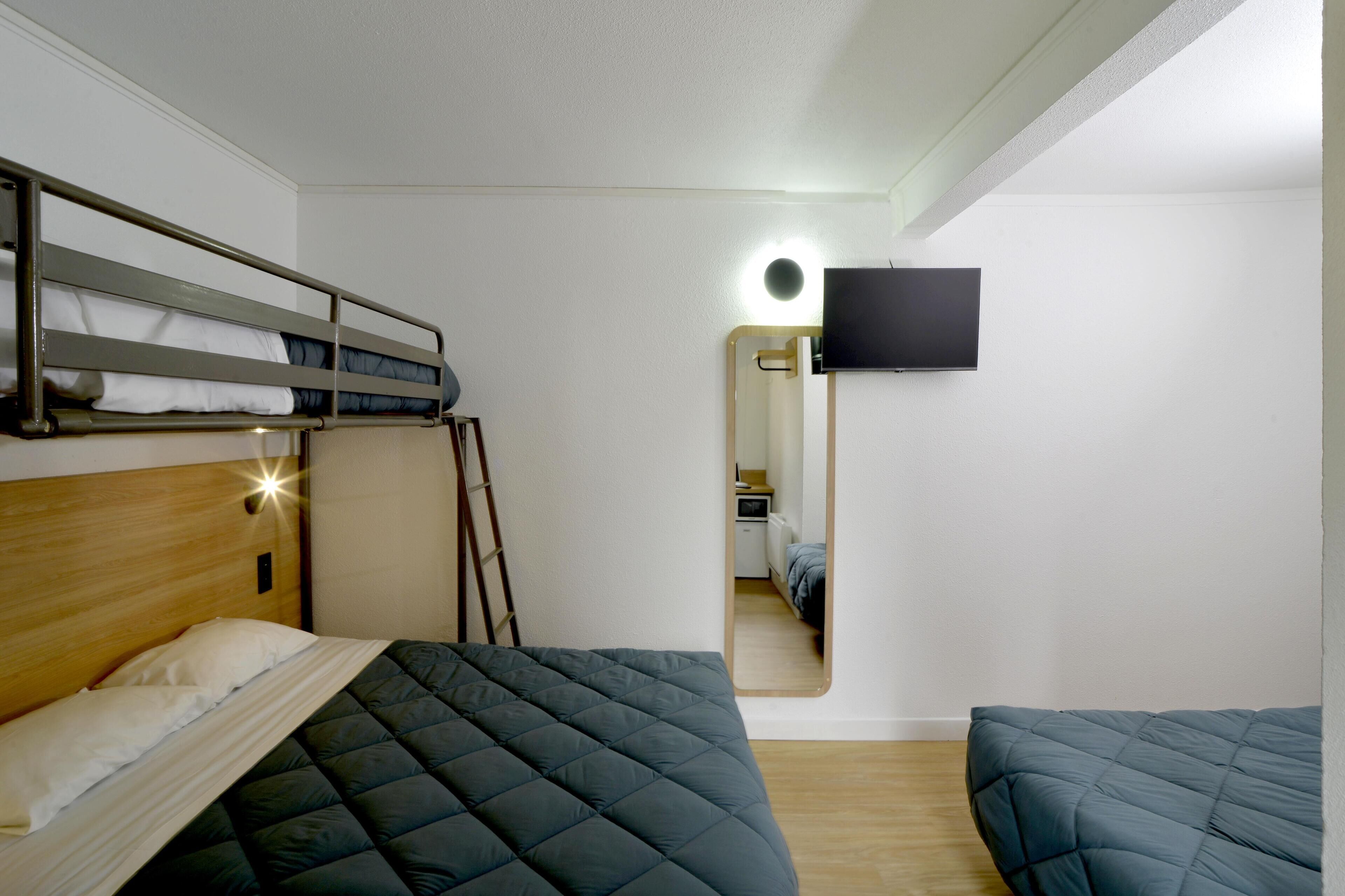 A room with bunk beds, a flat-screen TV mounted on the wall, and a mirror reflecting the room.