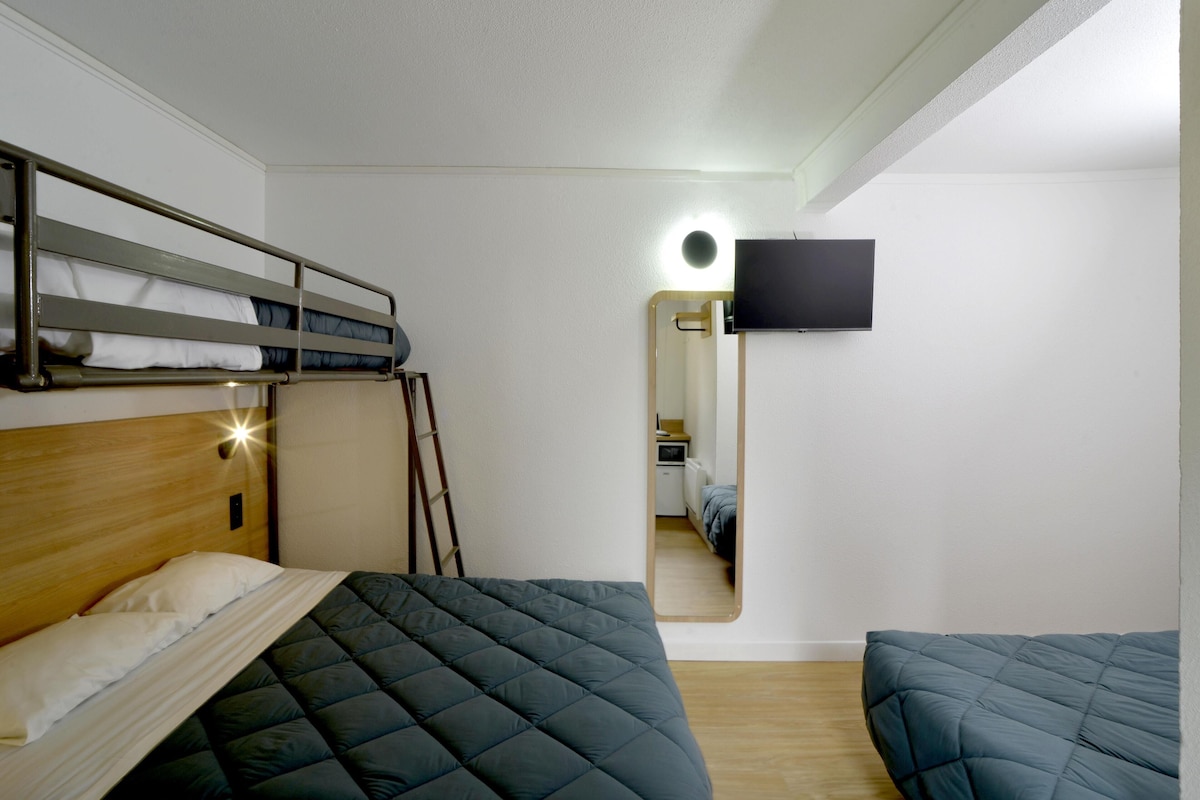 A room with bunk beds, a flat-screen TV mounted on the wall, and a mirror reflecting the room.