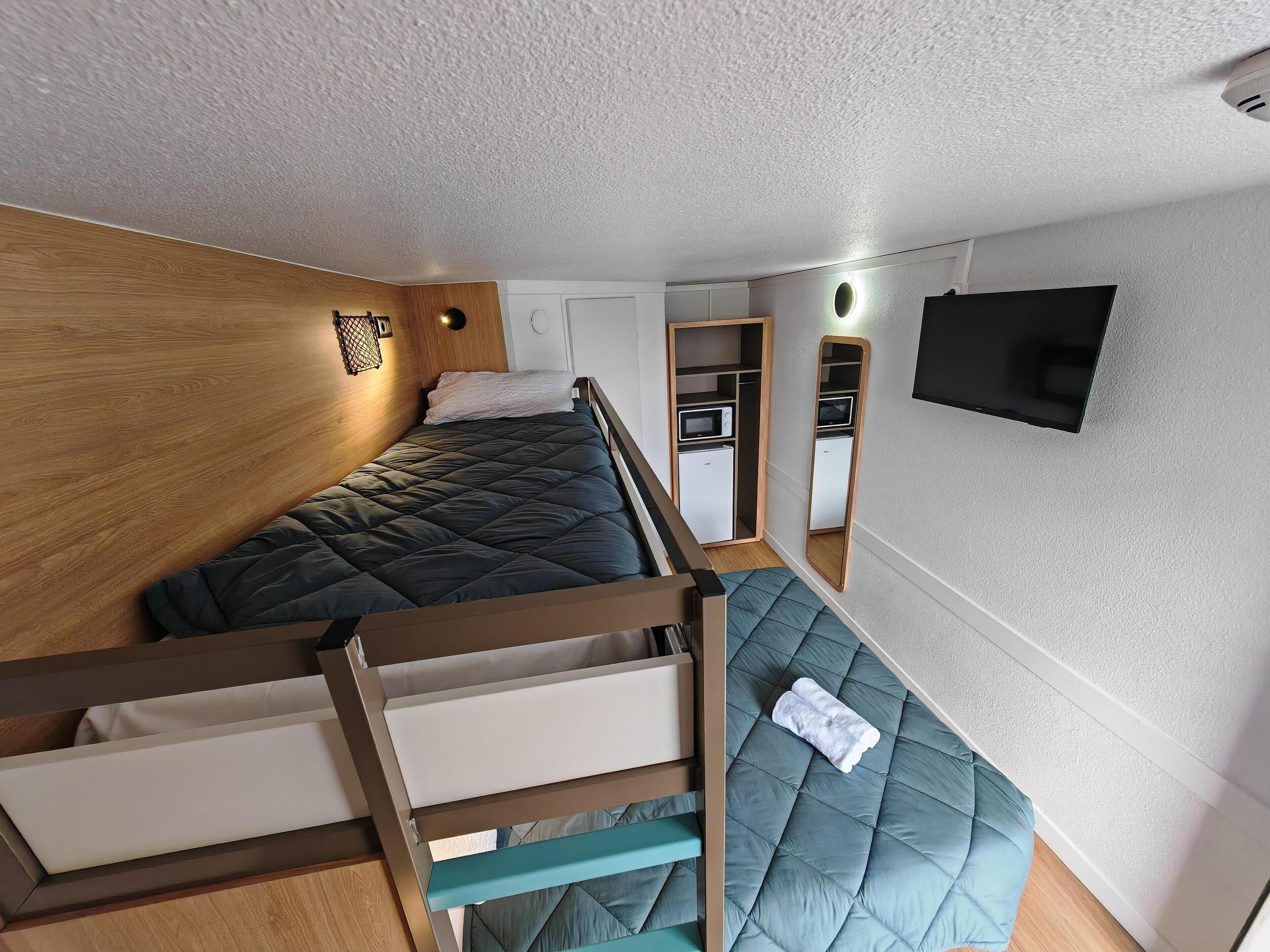 Une chambre compacte comprenant un lit superposé, une petite kitchenette, un miroir et un téléviseur.