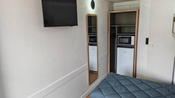 Ein kleines Zimmer mit Bett, Fernseher, einer Küchenzeile und einem Kleiderschrank.