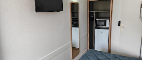 Une chambre de taille modeste comprenant un lit, un téléviseur, une petite kitchenette et une armoire.