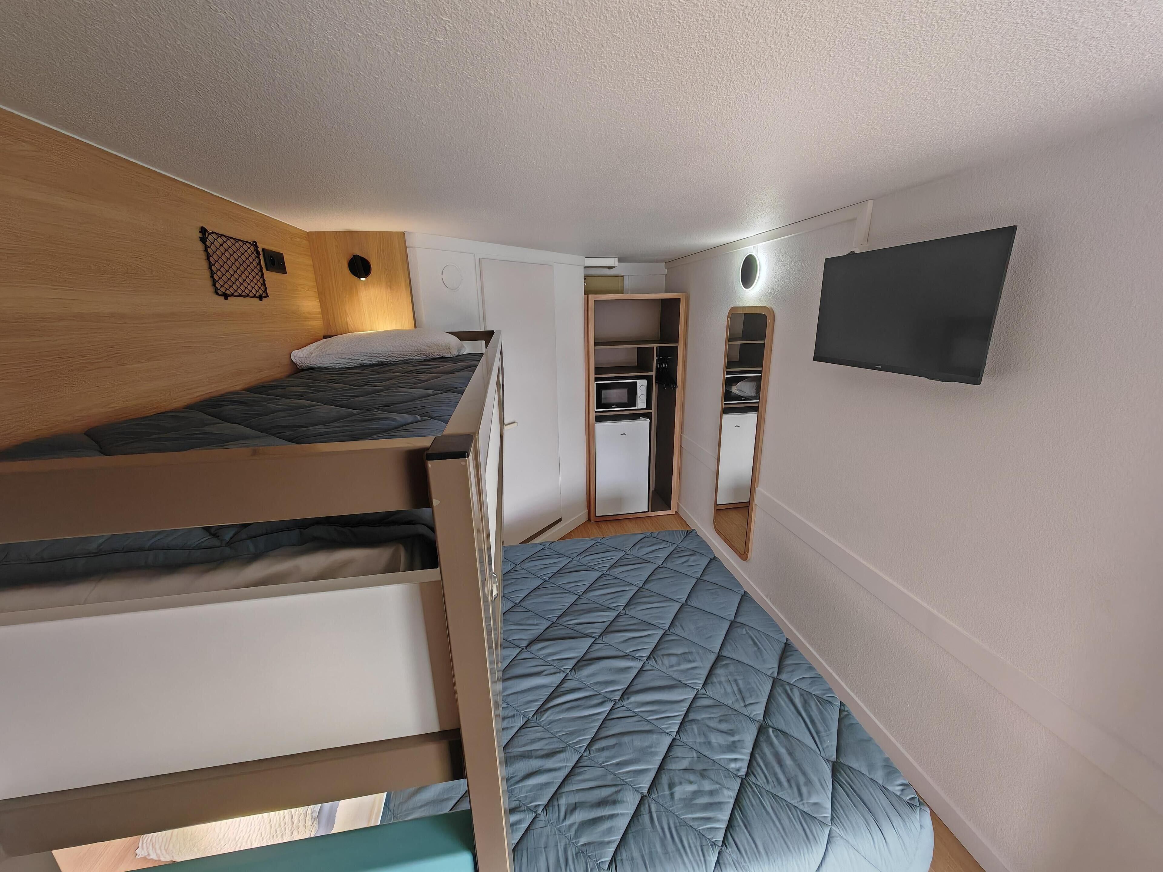 Une petite chambre avec un lit superposé, un coin cuisine et un miroir au mur.