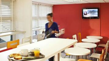 A cafeteria with a long table, chairs, and a television on the wall.